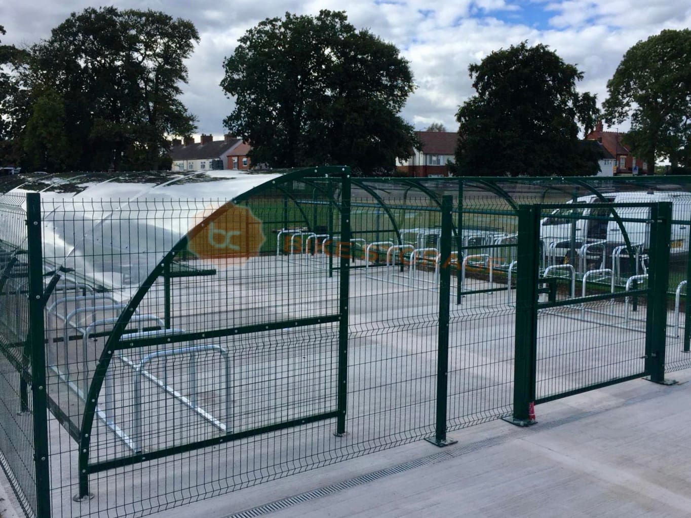 Modern black metal bike shelter installed behind mesh black gates outside of a school