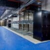 Two Tier Gas Assisted Bike Racks installed in an underground cycle storage facility next to a black cycle locker with blue flooring