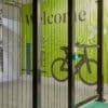 Our high security mesh fencing protecting a storage area with a green wall displaying the word "welcome" in large letters. The wall also features a graphic of a bicycle and directional arrows. The area appears to be secured with metal bars and has a locked gate.