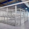 A large, well-lit room with industrial decor containing several rows of metal two tier bike racks enclosed by the anti-climb mesh fencing. The ceiling features exposed pipes and beams, and the floor is a smooth, polished concrete surface.