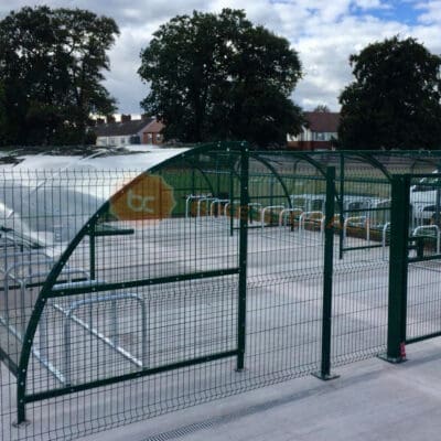 Modern black metal bike shelter installed behind mesh black gates outside of a school
