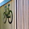 A black bicycle symbol mounted on a wooden slat wall, with part of the sign crossing over onto the slats, creating a clean, modern look.