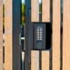 A keypad lock mounted on a wooden gate, showing a sturdy metal latch and a black keypad with buttons labeled with numbers and letters.