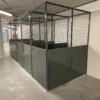 A spacious warehouse in the heart of a new building development features gray metal mesh security cages lined up in rows. Each cage has mesh walls and solid lower panels. The floor is clean, and the area is well-lit with overhead fluorescent lights.