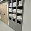 Towel station with 3 rows of shelving installed and several stacks of towels folded neatly on the shelves. The station is grey with slots for dirty towels to be inserted.