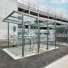 Modern outdoor bicycle parking facility with covered racks and glass windbreaks, designed for secure bike storage, located near a building.