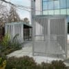 a bike rack and metal bike shelter behind a group of plants