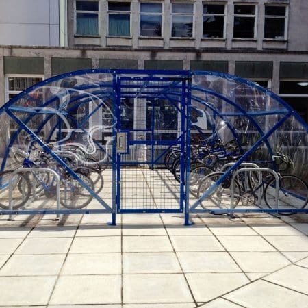 front view of the 20 space original enclosure with blue metal framing and mesh door installed outside a residence with bikes parked