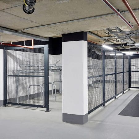 A modern, well-lit indoor bicycle storage area with metal 50mm x 50mm mesh security fencing and two tier cycle racks.