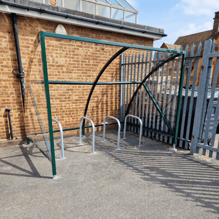 ral green original cycle shelter with 4 sheffield stands outside in front of wooden fence