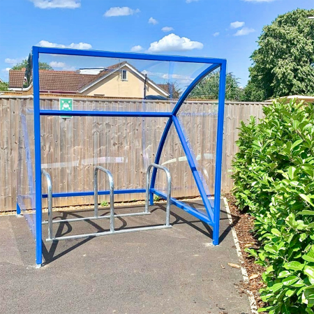 ral blue original cycle shelter with 3 sheffield stands outside in front of fence