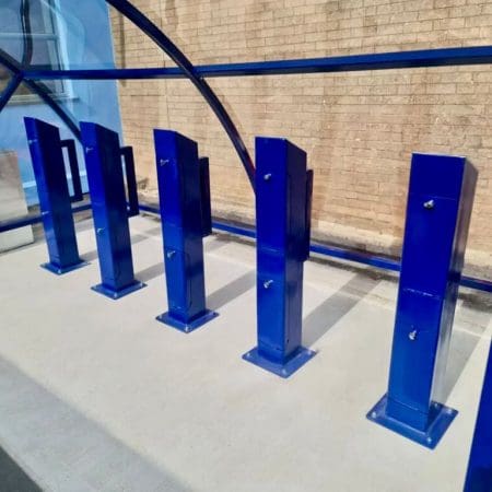 A row of blue e-bike charging stands installed outside under a blue polycarbonate bike shelter