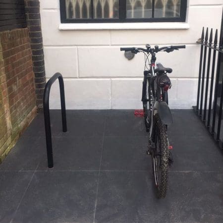 Two Sheffield Cycle Stands in RAL Black the stand on the right has a bike chained up and the rack is installed outside a residential property