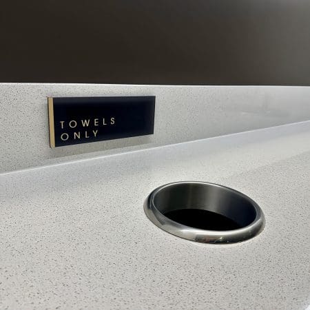 Close up of the towel station dirty towel slot in the white bench top with a sign displaying "towels only"