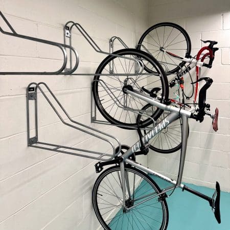 Vertical Bike Rack installed on a white brick wall in an underground bike storage facility, with two bikes on the right side being hung vertically
