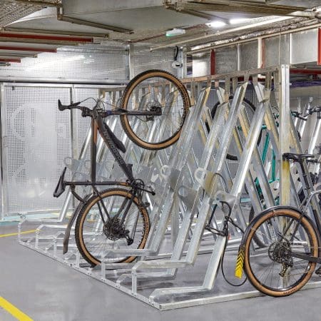 Semi Vertical Bike Rack installed in an underground cycle storage facility next to Perforated Mesh Fencing and two bikes being stored