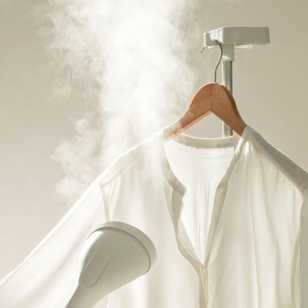 A neatly organized closet with several possessions hanging on black hangers. A peach-colored button-up shirt is prominently displayed, along with a gray pair of trousers draped over the hanger. Dark suits and other clothing items hang in the background, all benefiting from versatile storage solutions.